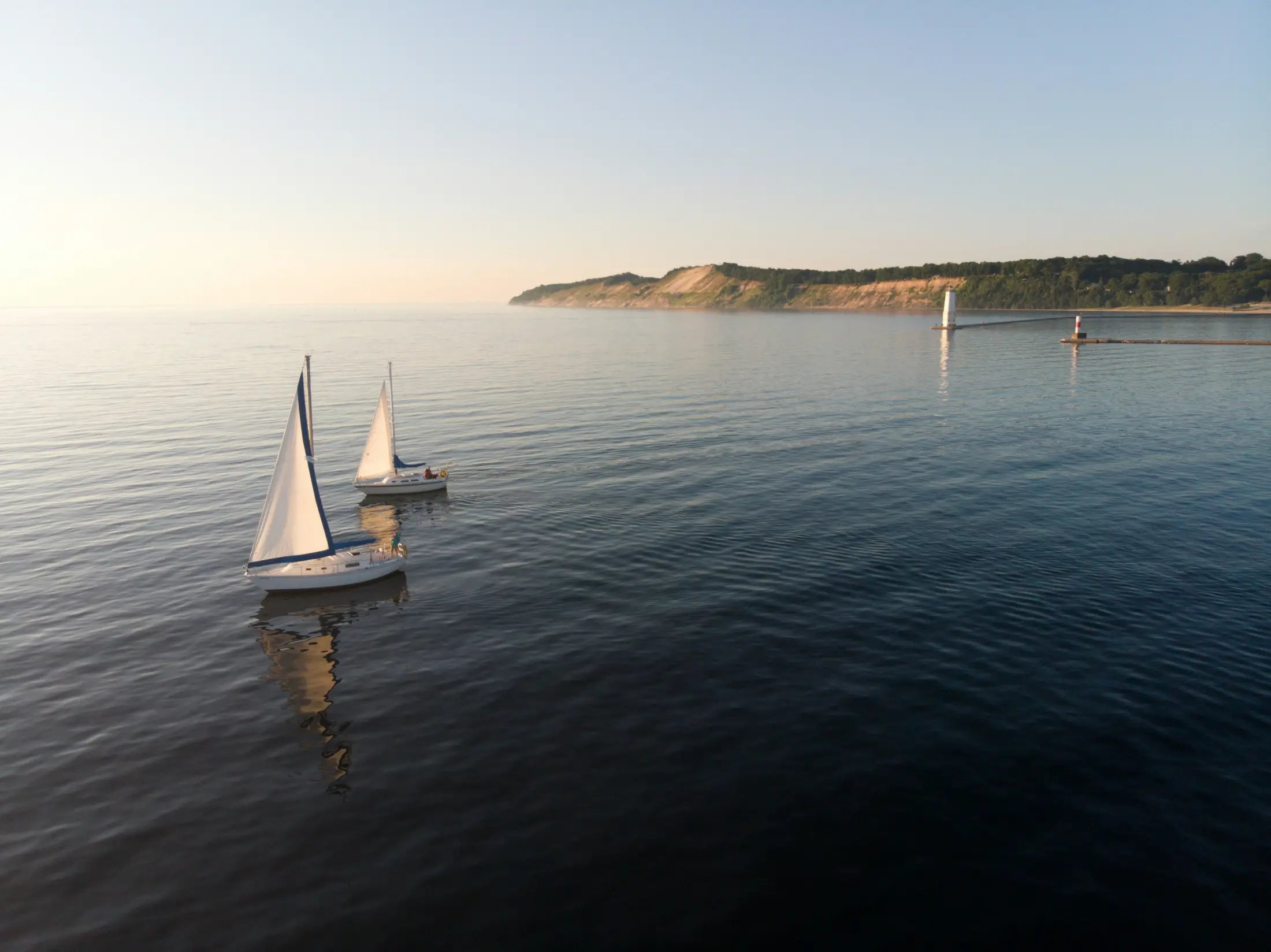 Two sailboats glide on calm blue water near a coastline with cliffs, greenery, and a sunset sky—an inspiring scene to reflect on your savings rate.